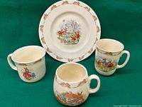 Four pieces showing plate with running rabbit border and three Bunnykins cups with various Bunnykins scenes celebrating Gold Jubilee