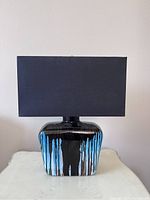 Front view of ceramic table lamp showcasing its glossy black base with blue drip glaze and black rectangular fabric shade.