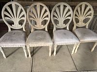 Front view of the four dining chairs showing carved oval backs and upholstered seats with stains and signs of use.