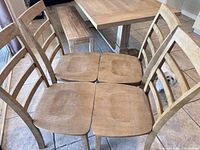 Four wooden dining chairs arranged around a wooden dining table showing ladder-back and contoured seats.