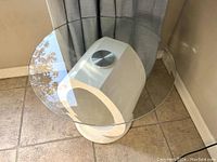 Photo showing the round glass top and white sculptural circular base from above and side angle.