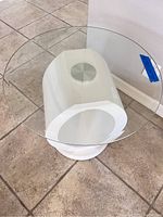 End table with a round clear glass top and white sculptural base shown from above at an angle.