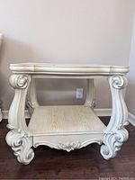 Front view of the square white end table showing detailed scroll carved legs and a wood grain finish shelf below the top.