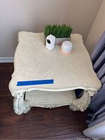 Front top view of the white end table with decorative legs and items on top.
