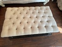 Top view of tufted beige fabric surface of the ottoman table showing button details and stains.
