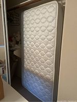 Single white quilted mattress standing vertically against a wall, showing detailed hexagonal and diamond stitching on the surface.