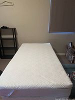 Full view of single size mattress covered with white mattress topper on top.