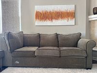 Front view of the three seated sofa showing cushioned seating and backrest with rolled armrests and a canvas painting on the wall above it.