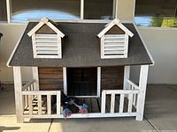 Front view of wood dog house showing porch, front entry, and dormer windows on roof.