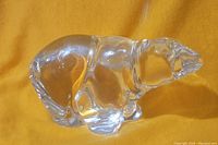 Side view of clear crystal polar bear figurine showing detailed body contours and polished finish placed on yellow background.