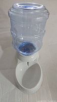 Front view of the large pet water dispenser showing clear blue plastic reservoir screwed onto white base with drinking bowl.