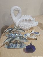 White swan, dolphin figurines, unicorn and blue glass decor pieces on wooden surface