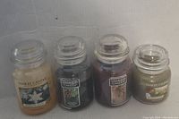 Four used Yankee Candle jars with clear lids shown on a surface, varying amounts of wax, with labels visible of Sparkling Snow and other scents.