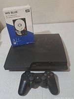 Photo showing the black Sony Playstation 3 console with a DualShock 3 controller placed on top and the WD Blue new 1TB hard drive box beside it.