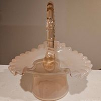 Photo of the Fenton pink overlay glass basket showing the ruffled edge and clear textured handle from the front angle