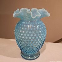 Front view of vintage Fenton blue hobnail vase with ruffled top, showing hobnail texture and opaline blue color.