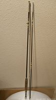 Three-piece vintage fishing rod standing upright, showing entire length including cork handle and rod tips.