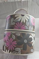 Front side of the vintage mid century floral hat case showing the flower pattern, zipper, and handle with cream trim.