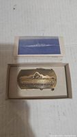 Belt buckle featuring USS Iowa BB 61 displayed in original box alongside a folded paper with ship image.