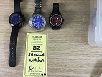 Three Android quartz watches placed side by side on a wooden surface showing different dial colors and band materials.