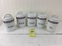 Full front view of five white ceramic canisters labeled Farina, Barley, Sugar, Coffee, Tea with floral border and gold trim lids on white wooden surface.