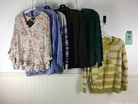 Six women's tops hanging on wall showing various colors and styles including floral, knit, and jacket pieces.