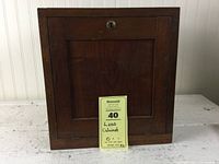 Closed antique wooden cabinet with a keyhole on the front door and a dark walnut finish