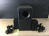 Front view of the bass module with two cube speakers and tangled wires to the sides.