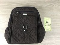 Front view of the brown Vera Bradley quilted backpack showing flap pocket, zippered pocket, side pockets, and silver hardware on light wood surface.