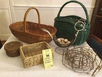 Front view of entire lot showing large oval basket, dark green basket, small round basket, rectangular basket, wire chicken basket with wooden eggs, and twig garland spread out on table.