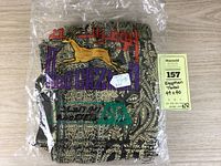 Packaged woven Egyptian throw with colorful branding logo including gazelle and Arabic text on black and beige patterned fabric.