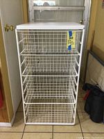 Full front view of white Elfa wire drawer unit with four baskets and solid top panel in a tiled room corner.