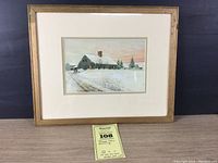 Full view of framed winter cabin painting with label in front