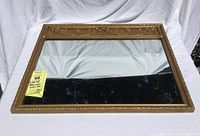 Full view of rectangular mirror lying flat, showing gold frame and reflective glass surface.