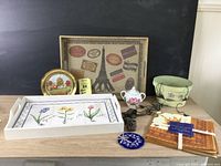 Various home decor items displayed on table, including trays, tin, sugar bowl, napkins, hooks, dish, glass ornament, and ribbons.