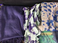 Full view of assorted scarves and shawls folded together, showing a range of colors including purple, mint green, yellow, beige, and blue animal print.