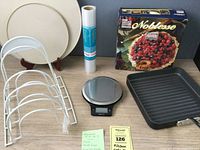 Full lot overview showing various kitchen items including scale, grill pan, tins, organizer racks, bake pans, shelf liner, and boxed pie crust.