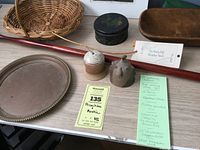 Overview of table displaying basket, bells, walking stick, painted tin, wood tray, copper dish, and handwritten description.
