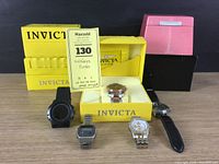 Collection of five watches displayed with four empty watch boxes: three yellow Invicta boxes and one pink Sunray box.