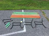 Overview of all bench components laid flat on ground showing wooden slats in green and orange paint, spare unpainted slat, and black metal bench frame parts with ground cleats and armrests.