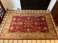 Full view of red and beige area rug laid on tile floor showing overall design and size.