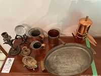 Photo showing the copper pan with brass handles, brass coffee set, iron decor with glass ball and brass candlesticks arranged on table