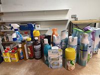 Photo showing multiple household cleaning and air freshening products including spray bottles, gels, and aerosol cans arranged on a table.