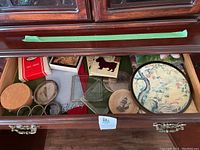 Open top drawer of dark wooden cabinet showing coasters, tiles, and trays with Asian floral and nature designs.