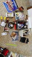 Overhead photo showing a spread of various miniature dollhouse items including boxes, miniature furniture, and a metal stove.