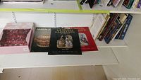 Three books placed on a white shelf, showing covers of La Moda Elegante and Fabergé book