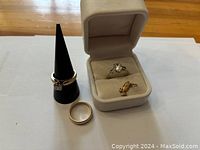 All items displayed: engagement ring in box, wedding band, white gold ring and gold charm