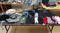 Table with a variety of hats, gloves, and slippers laid out, showing assortment of styles and colors