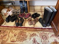 Photo showing ladies shoes and boots arranged on floor including black rubber boots, tan hiking shoes, red tweed slip-ons, and various sandals and casual shoes.