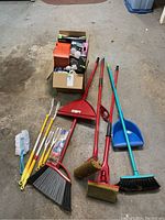 Full view of box with light bulbs and various cleaning tools including multiple mops, brooms, dustpans, and dusters.